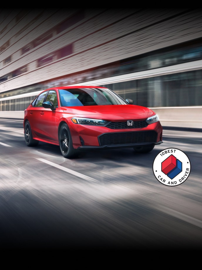 2026 Honda Civic Sedan Civic Sedan Sport in Rallye Red front view driving on a street with overlapping Car and Driver 10Best logo (Compact Sedan).