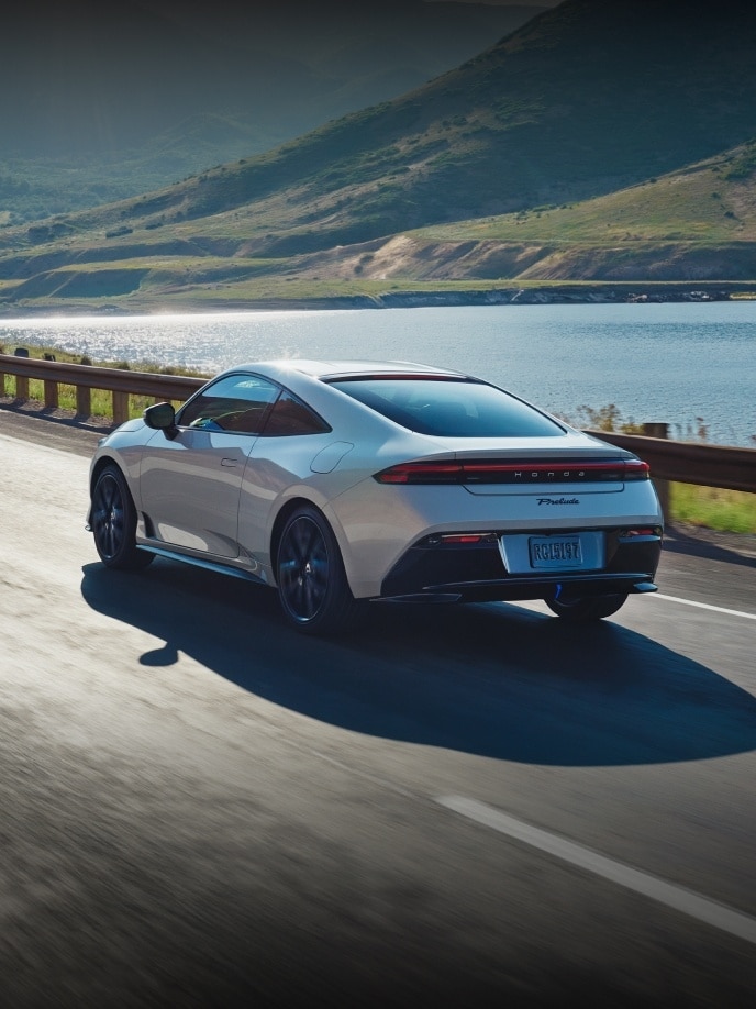 2027 Honda Prelude in Winter Frost Pearl, rear 7/8 view cruising alone the costal highway.