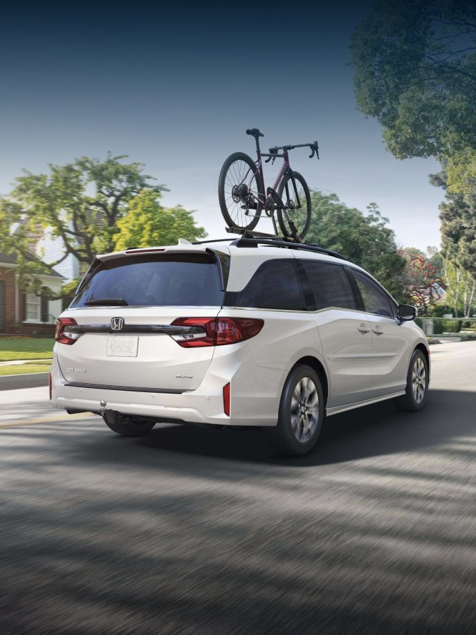 2027 Honda Odyssey Elite in Platinum White Pearl back driving through a sunny residential neighborhood (Minivan).