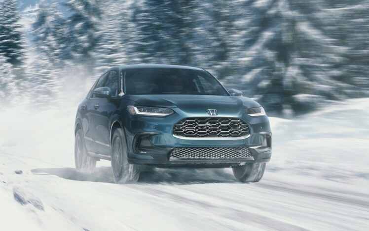 Front passenger-side view of the 2025 Honda HR-V EX-L in Nordic Forest Pearl, driving on a snowy forested trail.