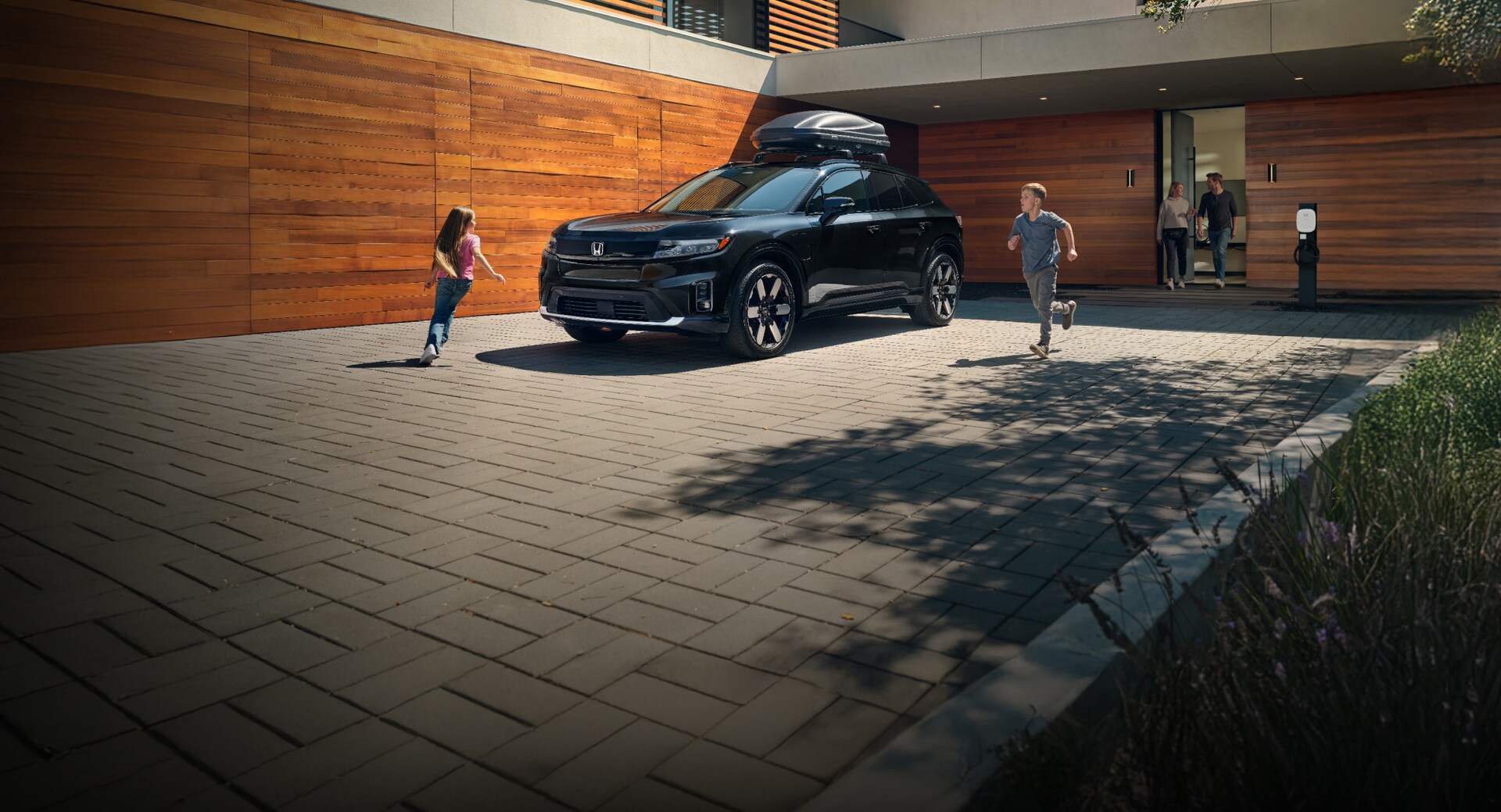 2026 Honda Prologue Elite in Raven Black, parked at home with Honda Genuine Accessories, while a few kids play around the car.