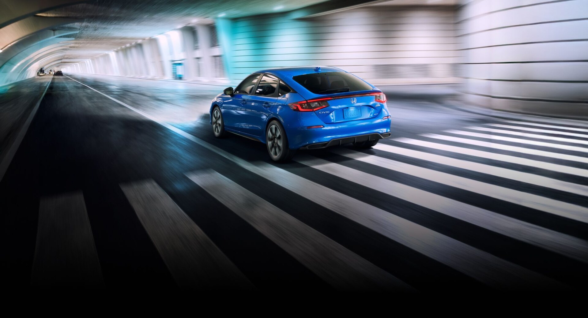 2025 Honda Civic Hatchback Sport Touring Hybrid in Boost Blue Pearl driving through underground tunnel.