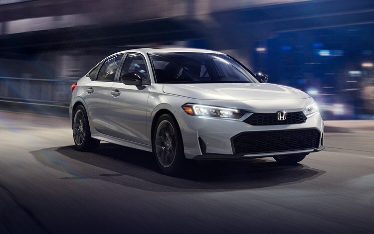 2025 Civic Sedan Sport Hybrid en Solar Silver Metallic driving in a city at night.