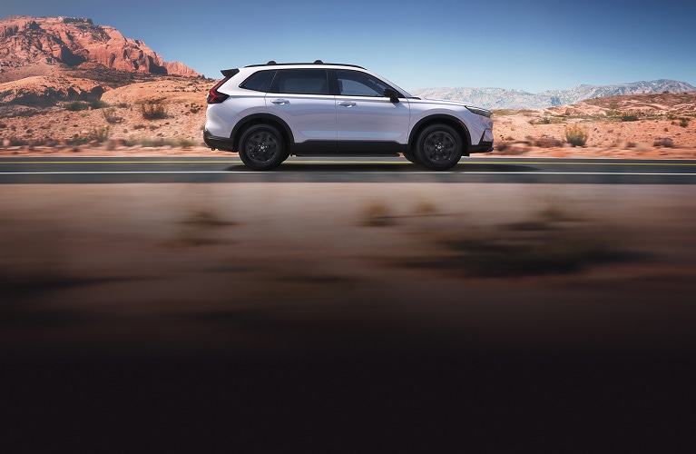 2026 Honda CR-V Sport Touring Hybrid in Platinum White Pearl profile driving on a scenic desert road (Compact Crossover SUV).