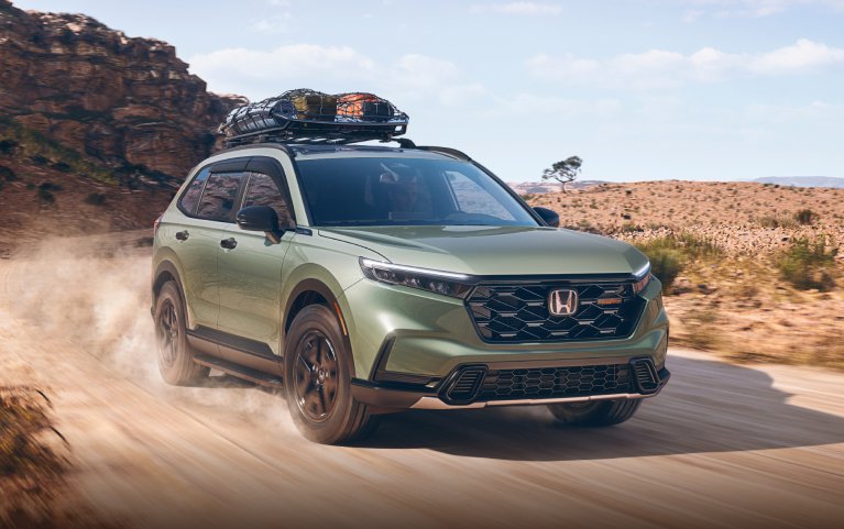 2026 Honda CR-V TrailSport Hybrid in Ash Green Metallic driving on a dirt road through desert national park landscape.
