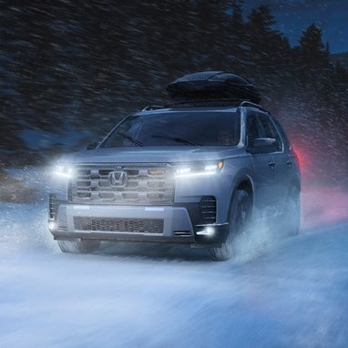 2026 Honda Pilot TrailSport shown in Platinum White Pearl with Honda Genuine Accessories driving in the snow