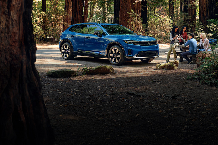 2026 Honda Prologue Elite in Pacific Blue Metallic, parked in a redwood forest, with people enjoying a picnic lunch.