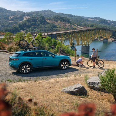2026 Honda Prologue Elite in North Shore Pearl, parked at a bridge overlook near a lake, with one bike attached to the roof, featuring Honda Genuine Accessories.