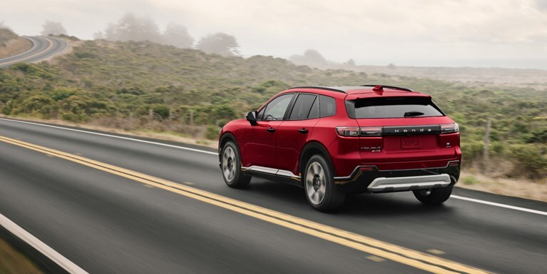 2026 Honda Prologue Elite in Scarlet Red Pearl, driving on a coastal road on a moody day.