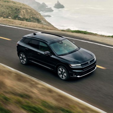 2026 Honda Prologue Elite in Raven Black, driving on a coastal road on a moody day.