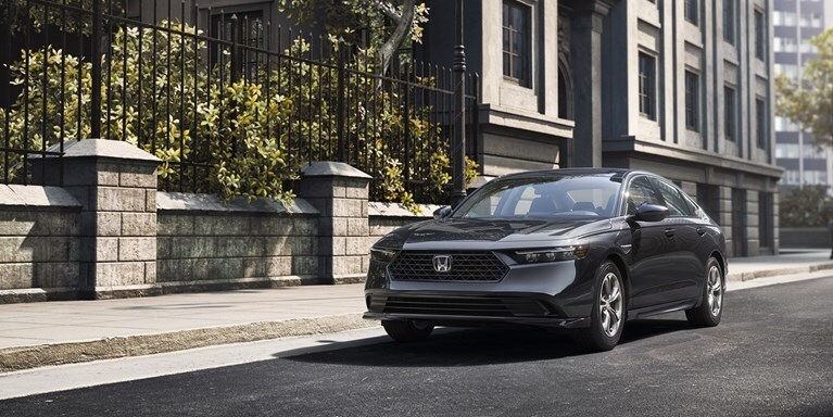 2026 Honda Accord in Meteorite Gray Metallic parked on the street next to a building and a city park with trees.
