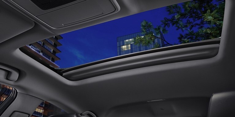 2026 Honda Accord detail of the one touch power moonroof parked on the rooftop of parking structure at night, with highrise buildings in the background.