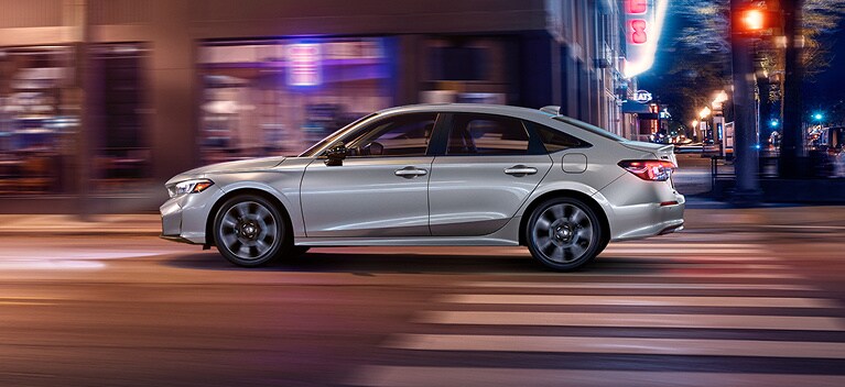 2026 Honda Civic Sedan Sport Touring Hybrid in Solar Silver Metallic profile driving on a city street (Compact Sedan).