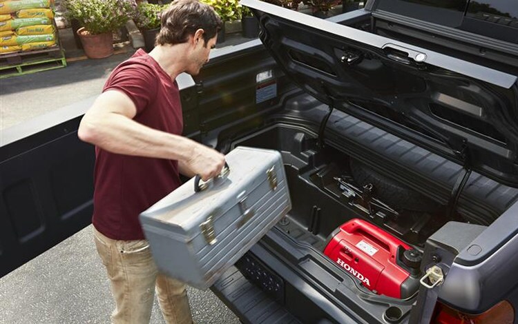 2026 Ridgeline RTL in Modern Steel Metallic Slight overhead shot of truck bed with tailgate opening, and a person is accessing locking in bed trunk with prop