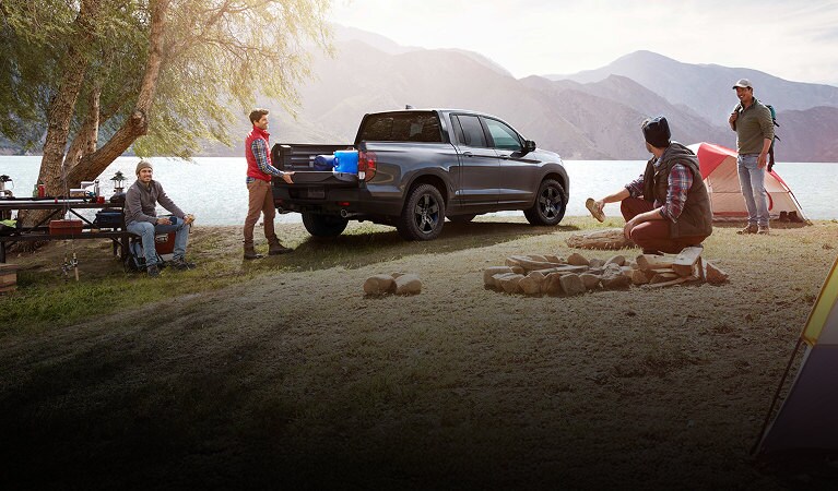 Ridgeline TrailSport in Modern Steel Metallic parked at camp site, lake in background, mountain in background, camp site, four men, building fire. Ridgeline TrailSport in Modern Steel Metallic parked at camp site, lake in background, mountain in background, camp site, four men, building fire.