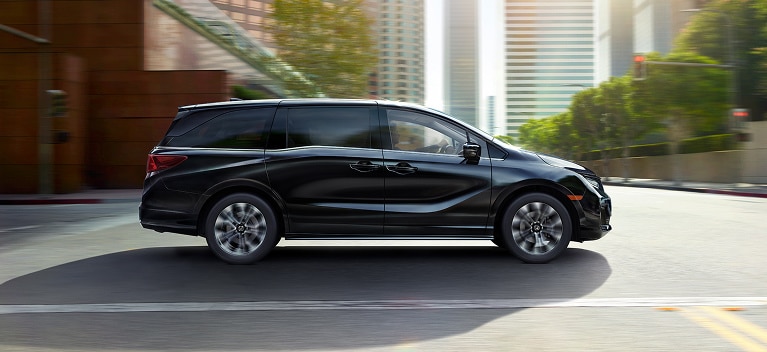 2027 Odyssey Elite family van in Crystal Black Pearl driving on a city street (Minivan).