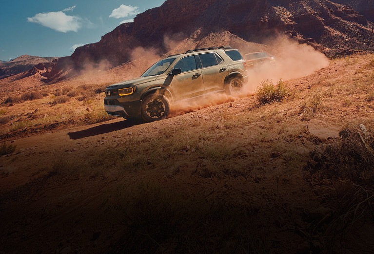 2027 Honda Passport TrailSport Elite in Ash Green Metallic profile driving on a dusty desert trail (Mid-Size SUV).